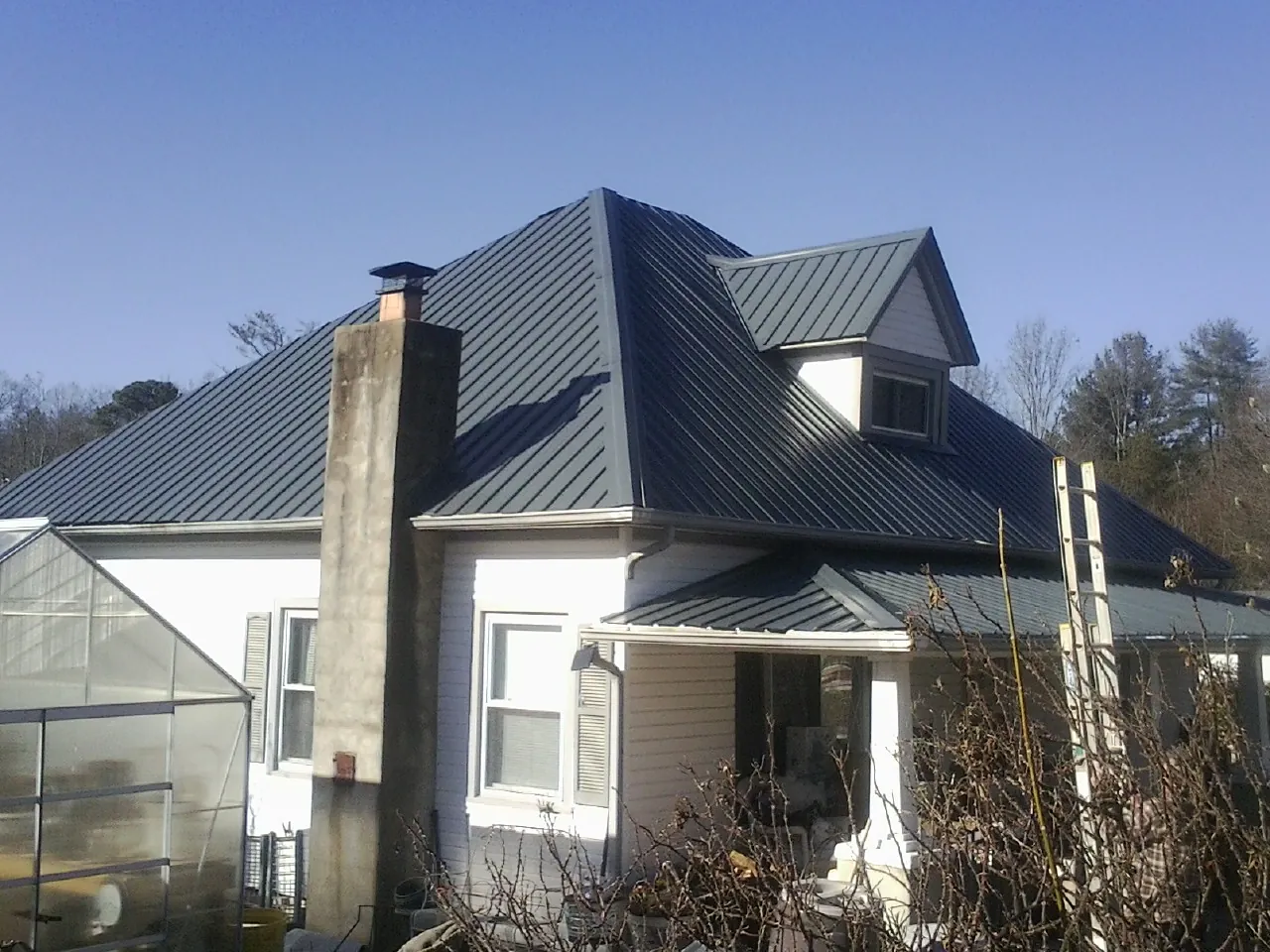 Dark blue standing seam metal roof on a white farmhouse with dormer — Slate & Tile Roof Repair by Roofing Brothers in Louviers