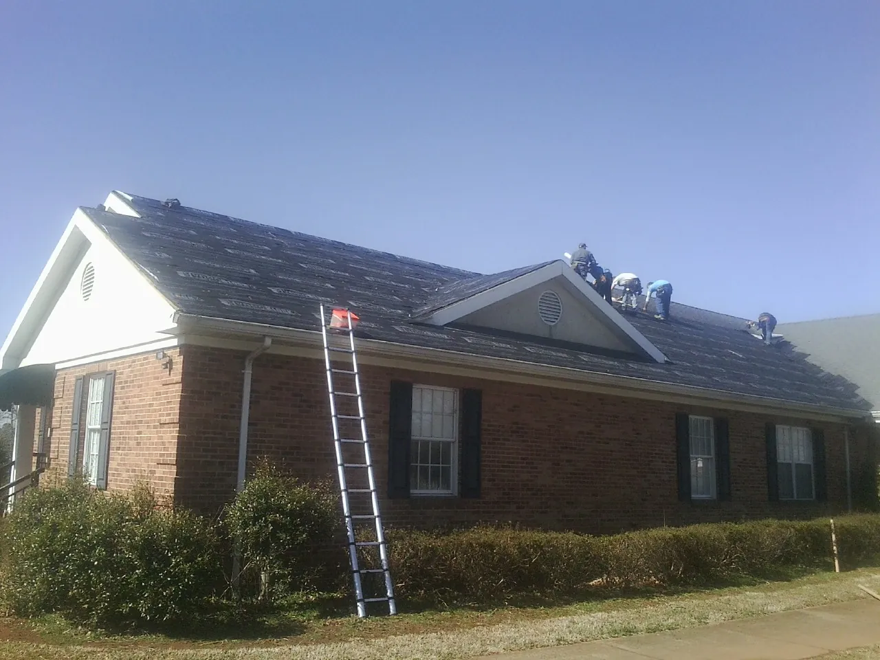 Crew tearing shingles off a brick ranch roof with a ladder set — Emergency Roof Repair work by our crew in Louviers