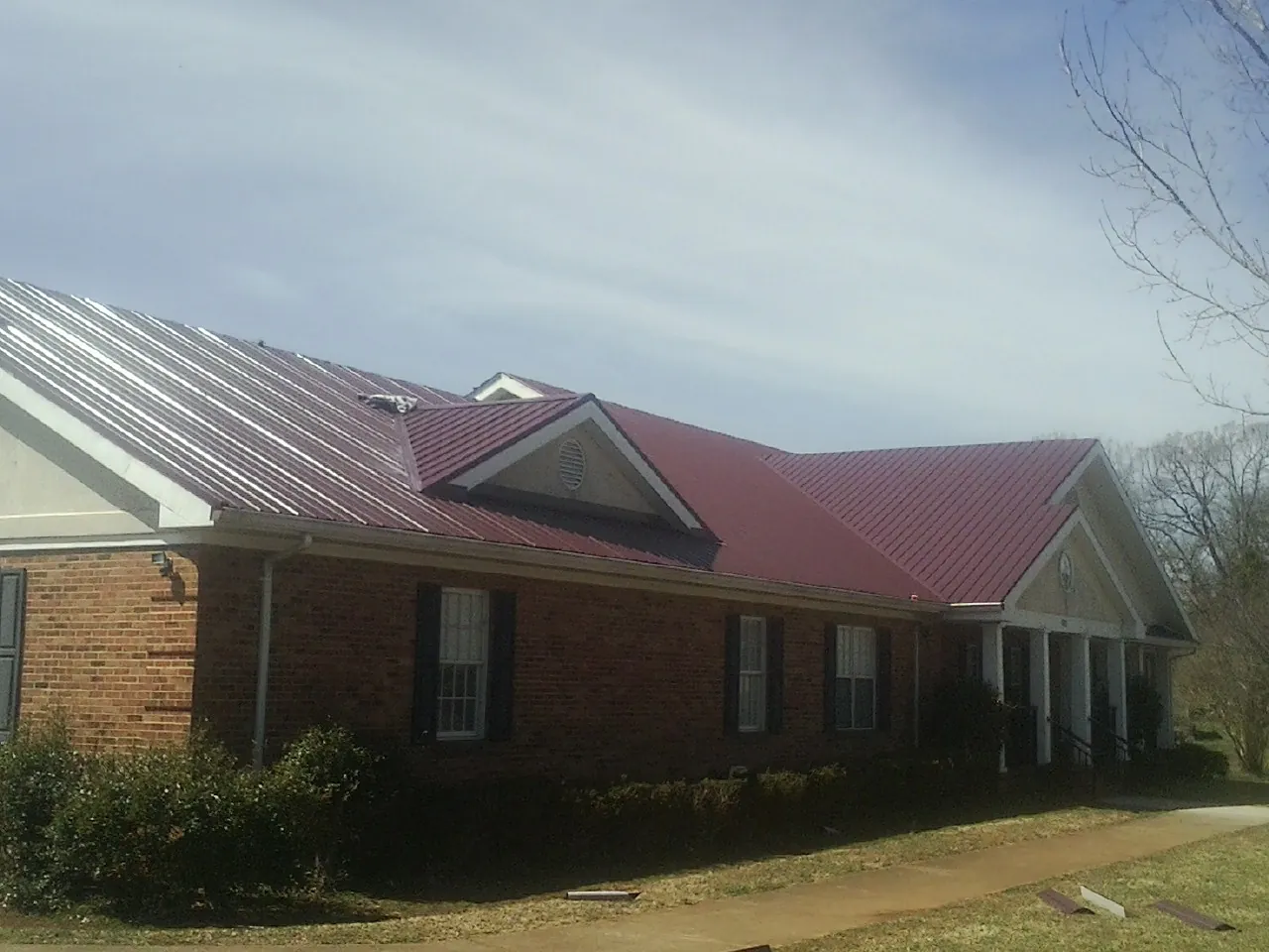 Red metal roof with gabled entries on a long brick building, from a Hail Damage Roof Repair job in Louviers