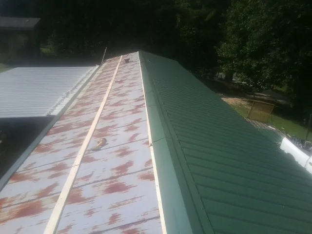 Old rusted panels beside newly installed green metal roofing — Wind Damage Roof Repair by Roofing Brothers in Louviers