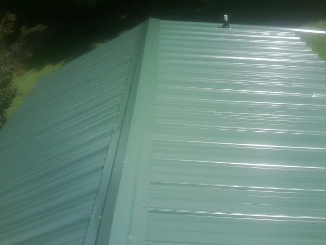 New green metal panels meeting at the ridge of a roof — Flat Roof Repair work by our crew in Louviers