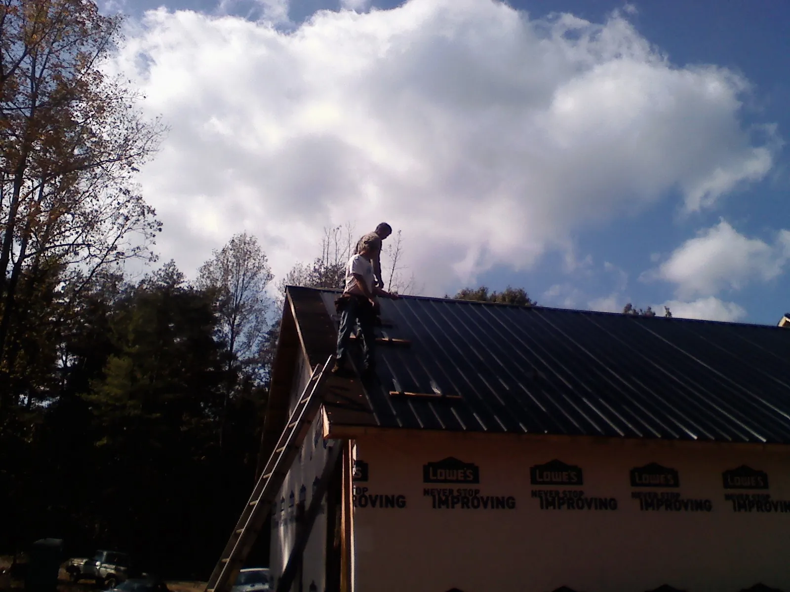 Roofer fastening dark metal panels high against a cloudy sky, from a Roof Inspection job in Louviers