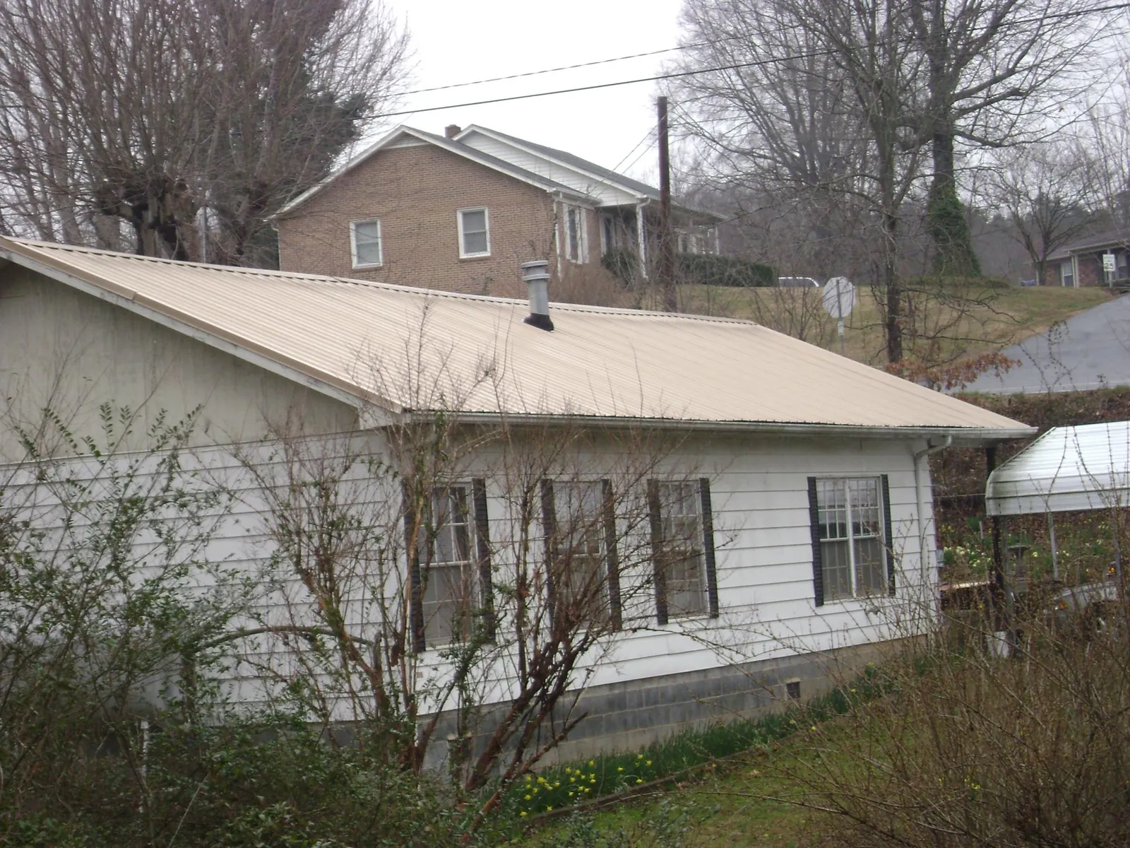 Tan metal roof on a white sided house set into a hillside — Commercial Roofing by Roofing Brothers in Louviers